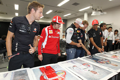 пилоты рассматривают постеры со своими автографами на Гран-при Японии 2011
