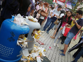 young man and woman eating kebabs next to filled trashcans at Dongmen