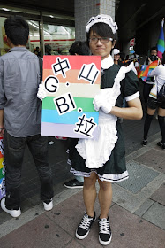 young man holding a sign and dressed up in a maid's outfit