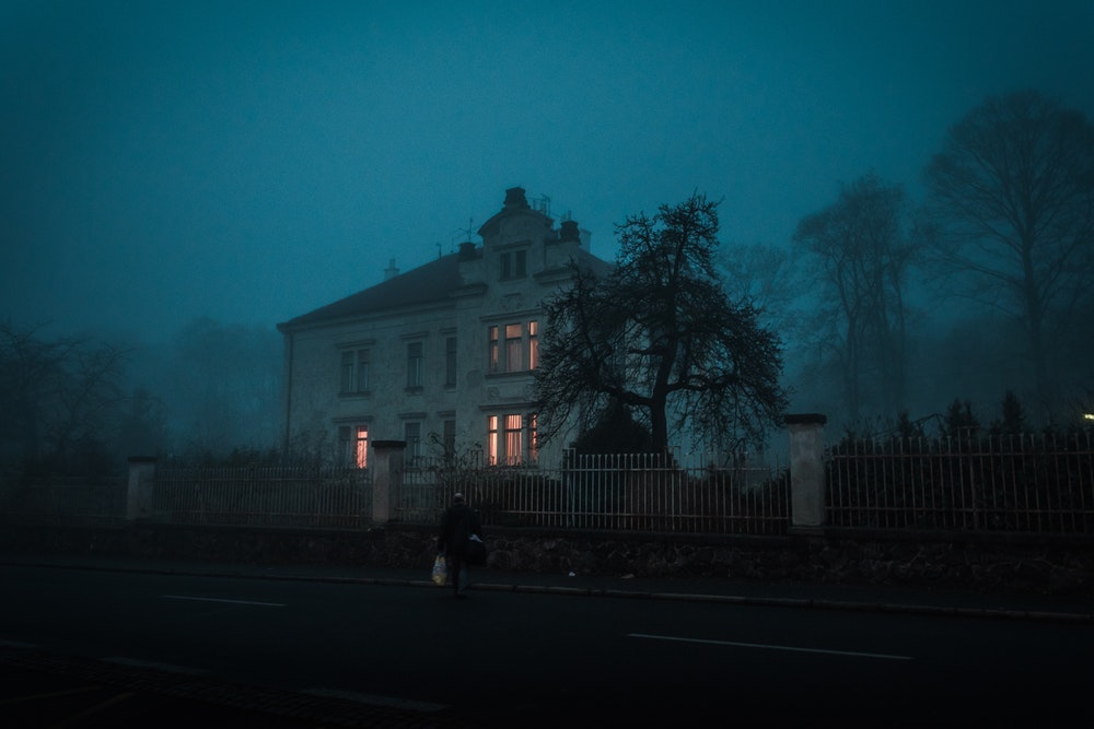 A person walking on a road with a scary mansion by the side in Psychiatrická nemocnice Bohunice