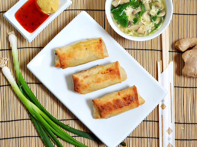 top view of three vegetable egg rolls on a white plate with dipping sauces on the side 