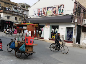 older man riding a bicycle past a building with images of fashionably dressed young women in Yangjiang, China