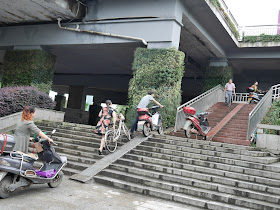 people pushing motorbikes up a steep stairway ramp