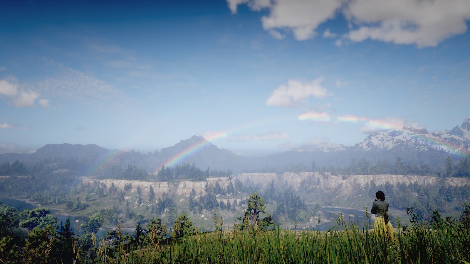 Tilly, standing at a cliff, looking out at the mountains with a double rainbow over them.