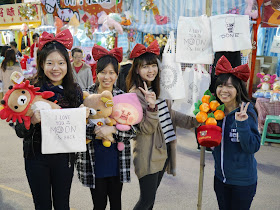 four female college students wearing large read bows on their heads and holding bags and stuffed toys
