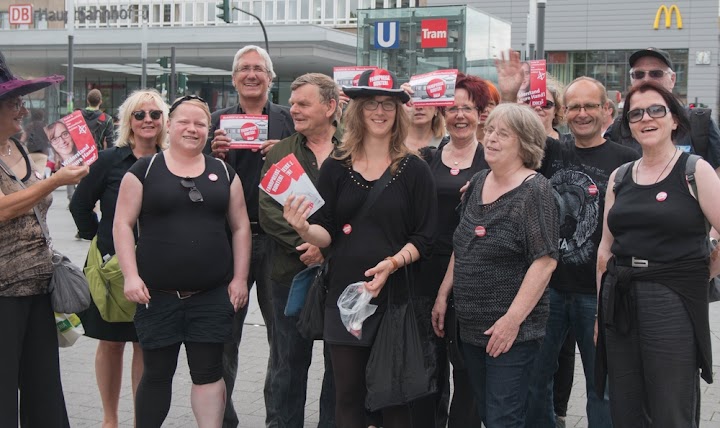 Genossinnen und Genossen, ganz in schwarz, mit Flyern.