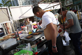 man with shirt lifted over his stomach grilling meat