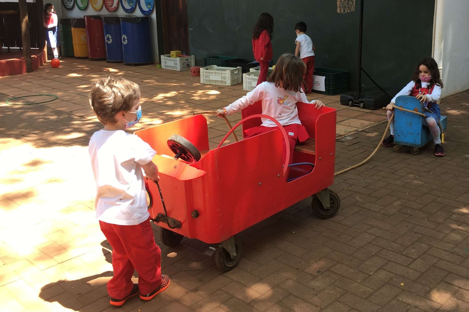 A imagem mostra 3 crianças brincando em um jipe vermelho.