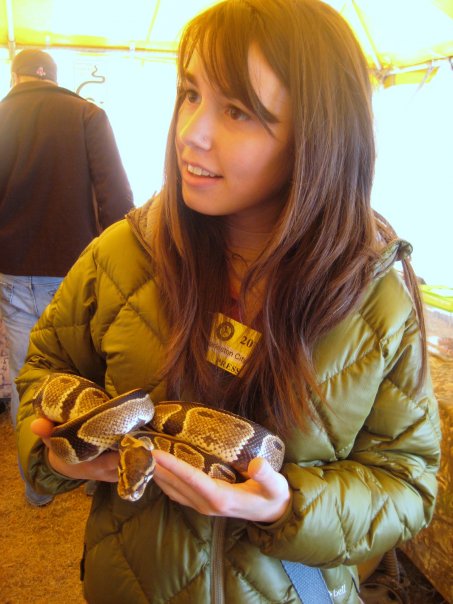A brown haired girl in a green jacket holds a snake