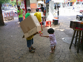 boy with a box over the top of his body and a barfeoot girl playing on a pedestrian street in Zhuhai, China