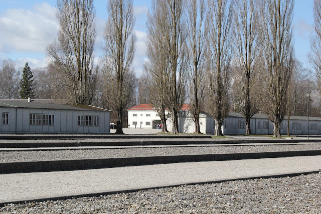Ślady po barakach obozu Dachau, widoczne dwa baraki zostały zrekonstruowane, w głębi brama z napisem „Arbeit Macht Frei”