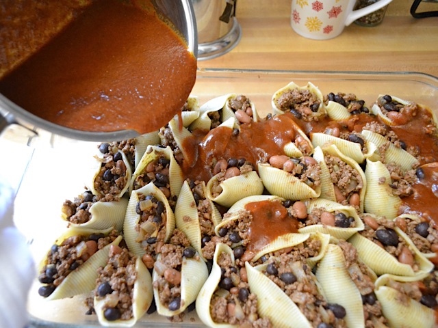 pouring enchilada sauce over top of filled shells 