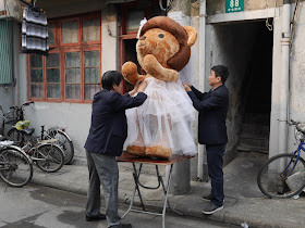 two men altering a wedding dress for a large stuffed bear