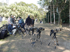 people near several professional cameras with large lenses on tripods near a wooded area at the Victoria Peak Garden in Hong Kong