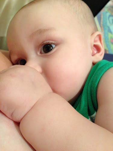 Calmly feeding. Big,dark eyes open and staring. Little hand covering breast.