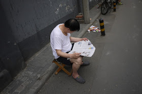 man reading a newspaper while sitting on a stool
