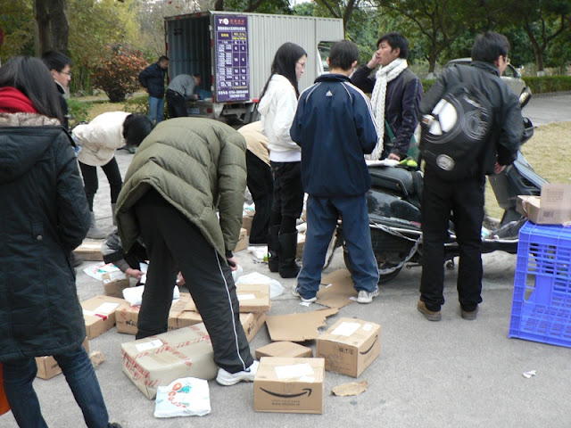 students picking up delivered packages sitting outside, several with Amazon.com logos of the boxes