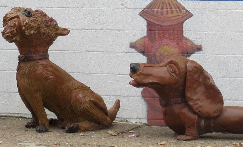 Two brown, concrete, dog sculptures.