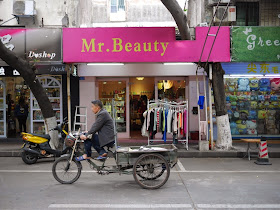 man riding a tricycle-cart past a store named Mr. Beauty