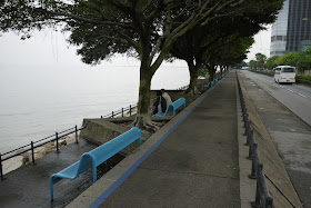 waterfront in Macau with 2 people sitting on a bench and an empty walkway