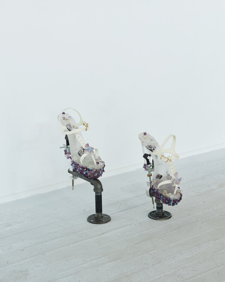 Image: An installation view of a sculpture by Sofia Moreno comprised of two embellished white jelly-plastic heels, supported by pipes on a gallery floor. Image by Ian Vecchiotti, courtesy of Hans Gallery.