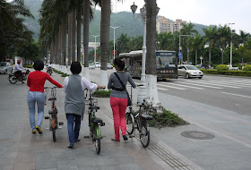 Three women pushing bicycles on a sidewalk in Zhuhai, China.
