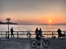 people looking at the sea and a biker riding by as the sun sets at the Cyberport Waterfront Park in Hong Kong