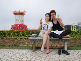 a young man and woman sitting on a bench at a park in Zhanjiang
