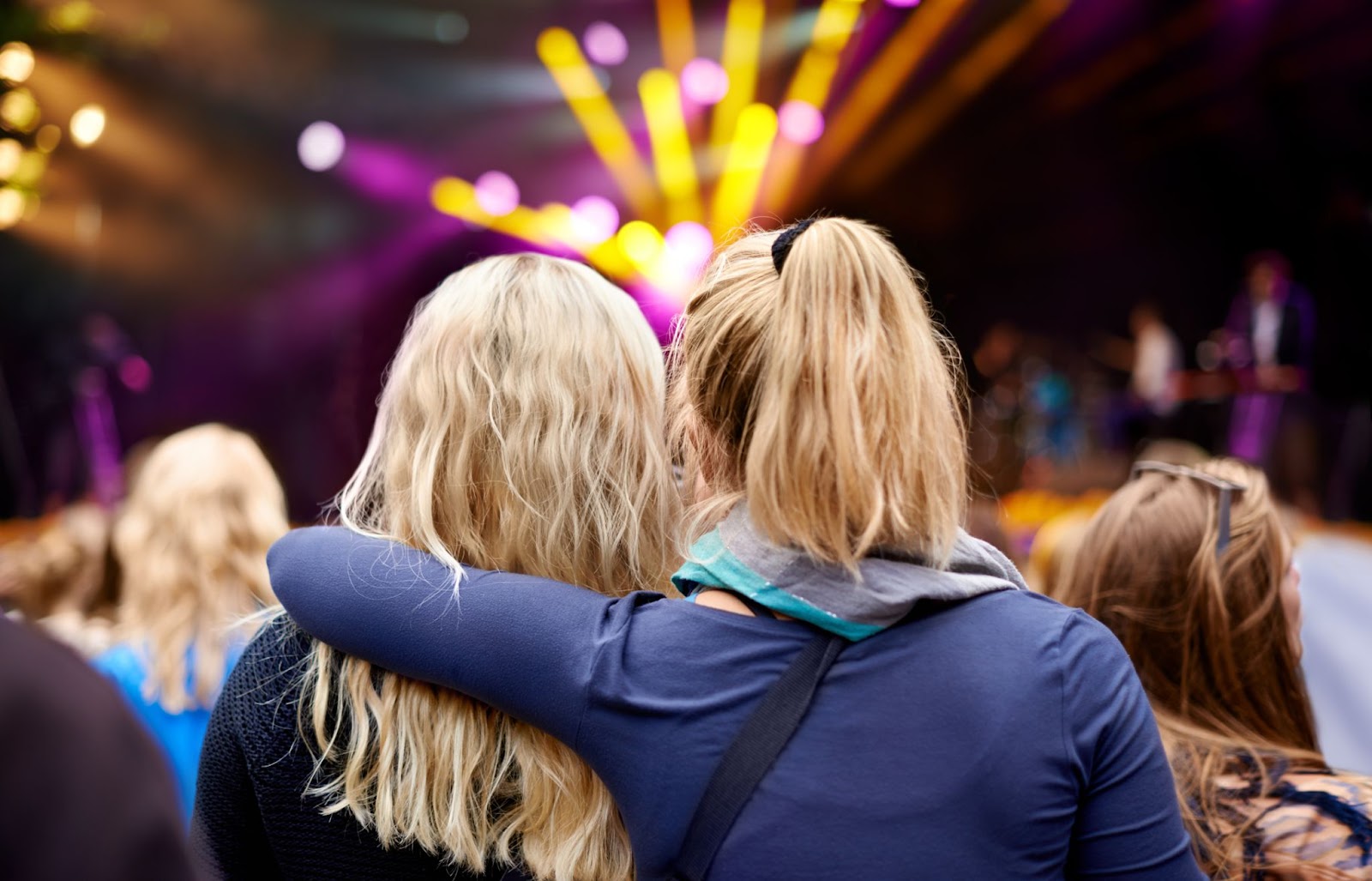 Two girls at a Taylor Swift concert, one with her arm around the other, sharing a moment. 
