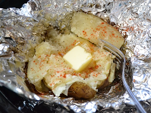 slow cooked potatoe in tin foil, cut open with butter on top and a fork on the side 