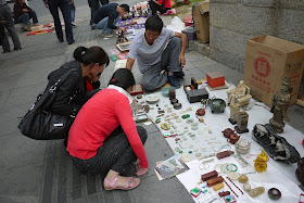 women squatting while looking at items on the ground for sale outside Tianxinge Antique City in Changsha, China