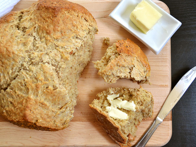 Brown Butter Soda Bread loaf with piece cut off and buttered and a dish of butter on the side with knife 