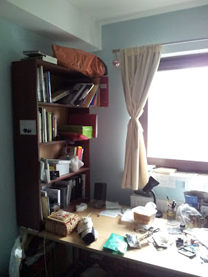 Shot of left-hand side of desk, with dark wood bookcase standing on it against the wall)