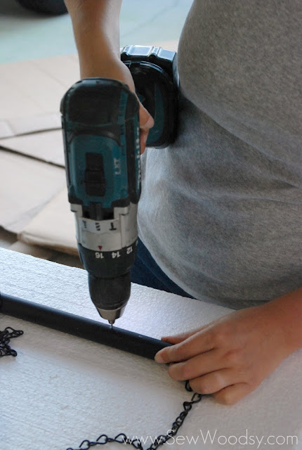 Female hand drilling a hole into a black piece of PVC pipe.