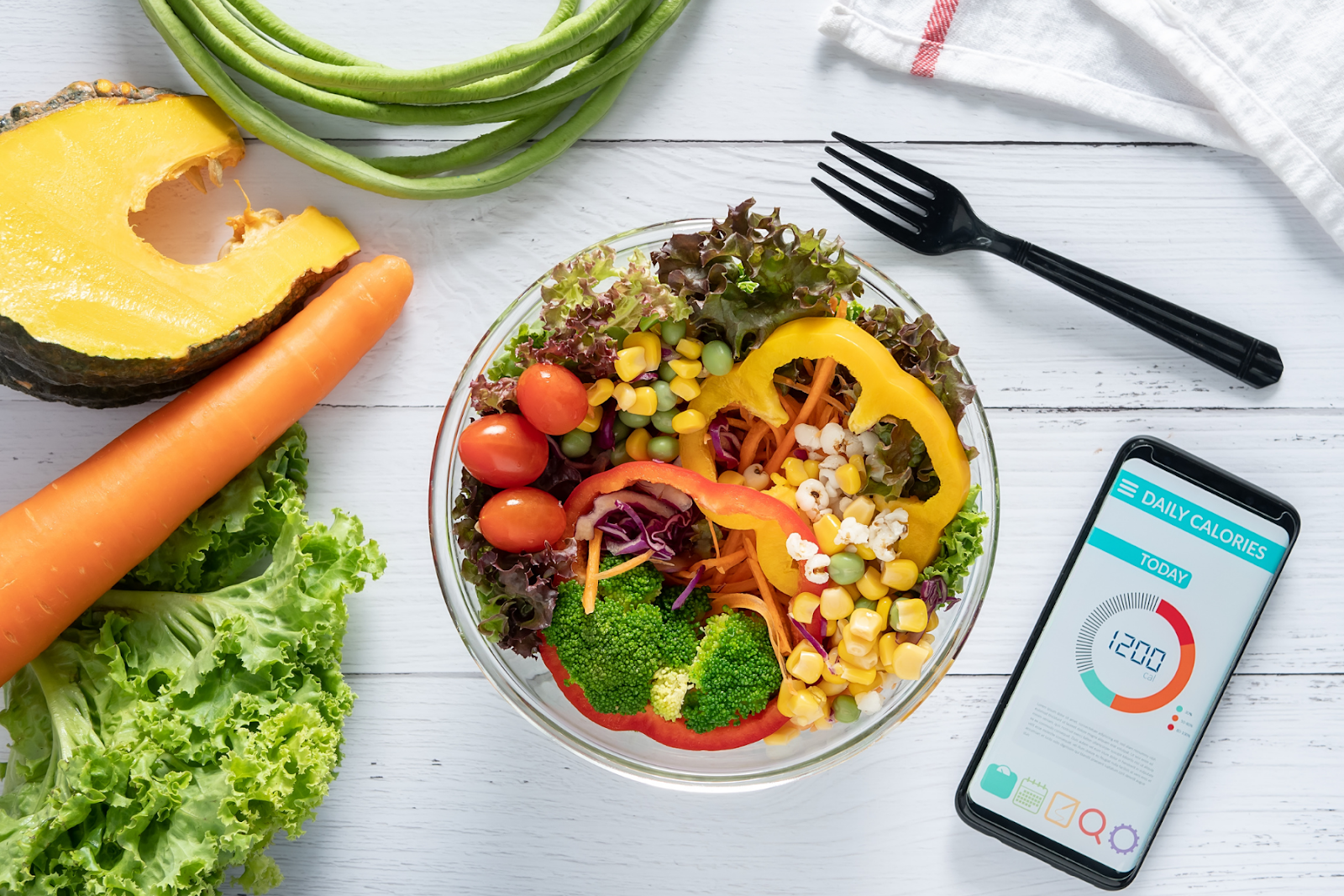 Overhead view of a bowl of salad and a phone with a calorie tracking app open reading 1200 calories. 