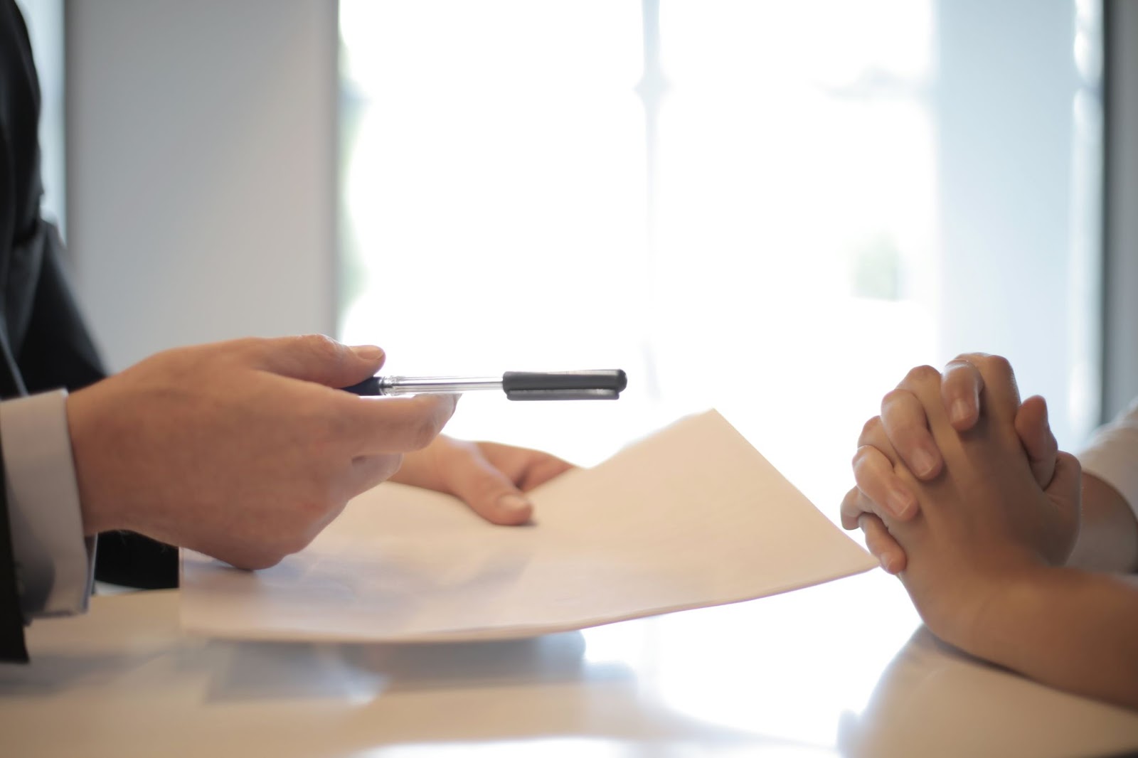 A close-up of two sets of hands, one handing a pen and paper to the other.