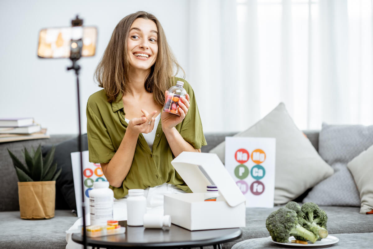 Influencer sitting on couch recording product review video behind iphone on camera stand: how to reach out to brands as an influencer