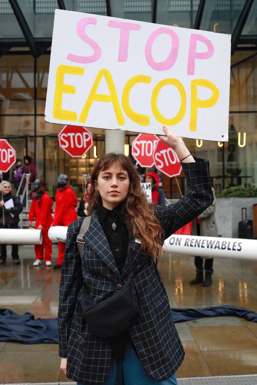 A young woman holds up a STOP EACOP placard