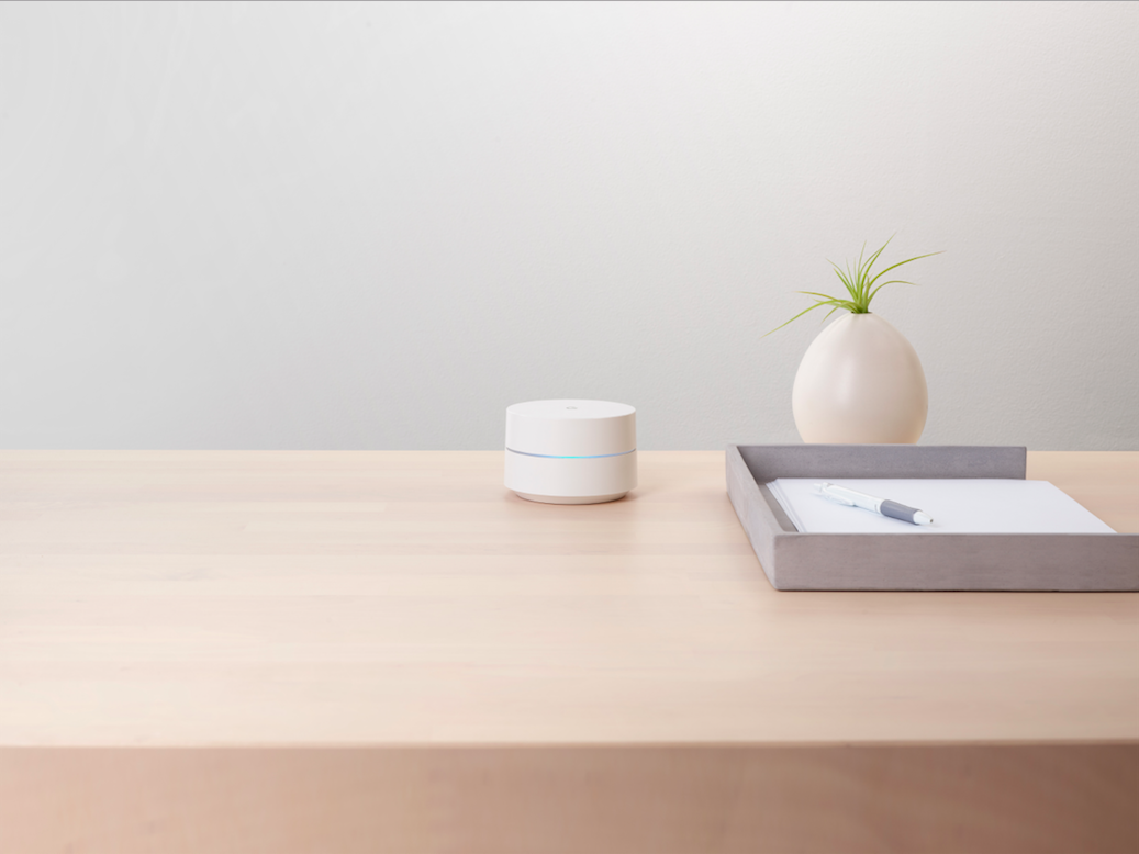 Un appareil Google Wifi est posé sur un bureau avec un stylo/papier et une plante