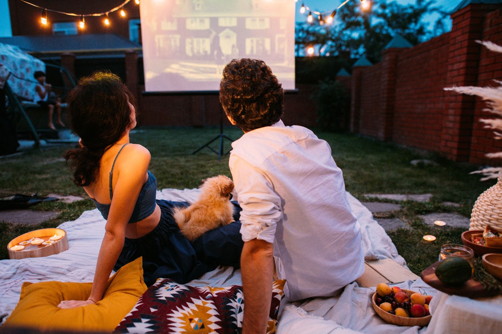 A couple watching a movie on a blanket in a backyard.