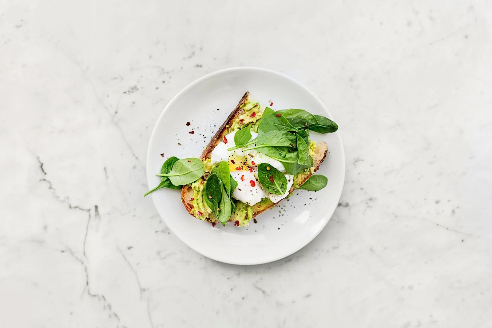 White plate of toast with an egg and spinach leaves.