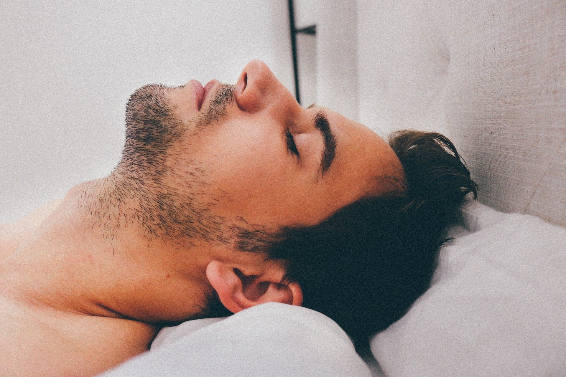 Man sleeping with his head tiled back on the top edge of the pillow