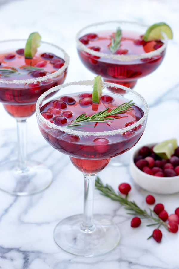 3 cranberry margaritas in glasses rimmed with sugar and garnished with lime and rosemary