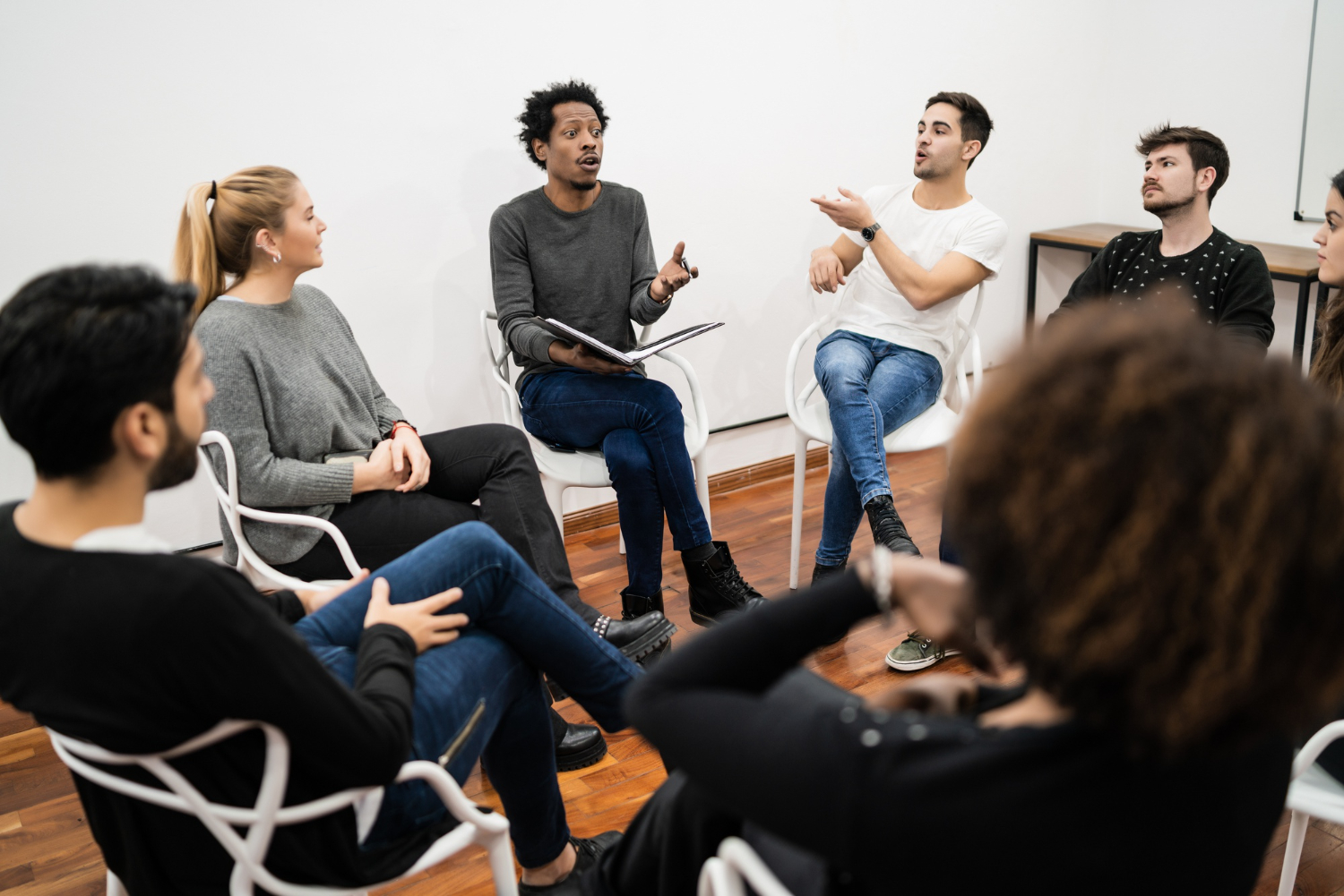 A imagem mostra um grupo de pessoas sentadas em cadeiras posicionadas em formato de um círculo. Essas pessoas parecem estar discutindo assuntos importantes em uma reunião de trabalho.  