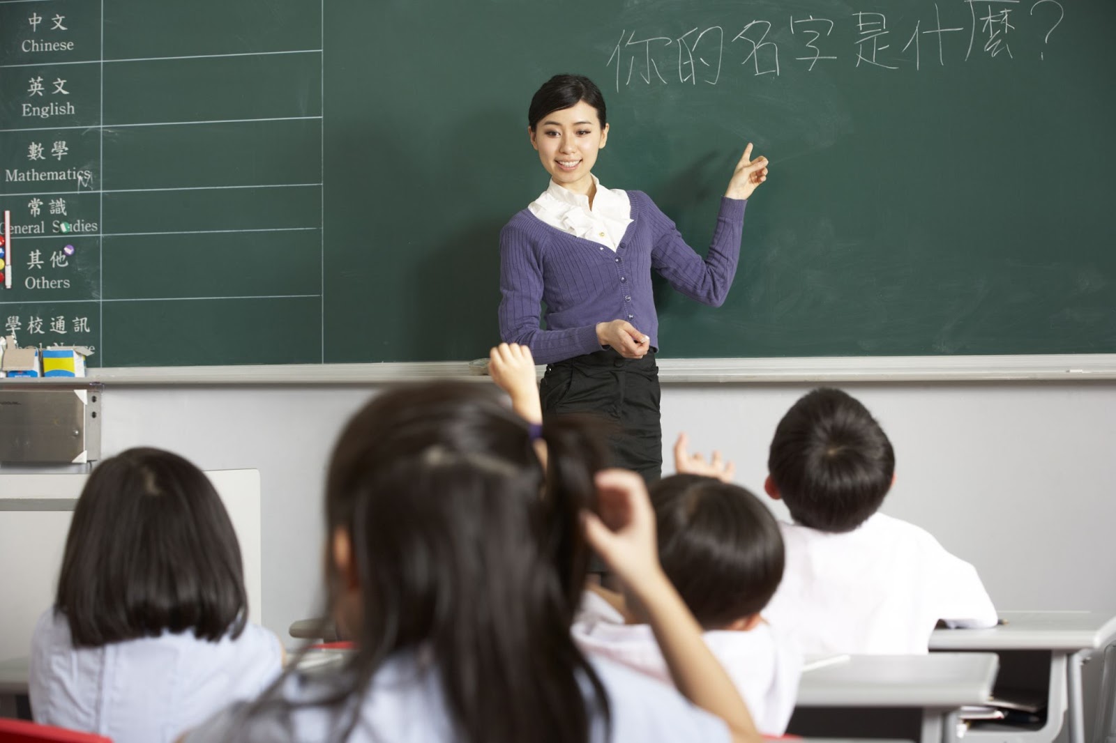 teacher standing beside the blackboard teaching students Chinese.