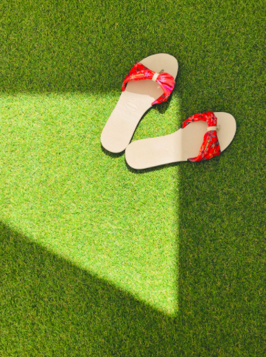 sandals with red bow on grass with sunlight