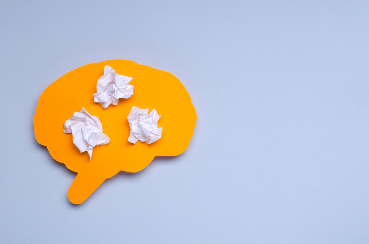 Orange cutout of a brain with crumpled pieces of paper inside it