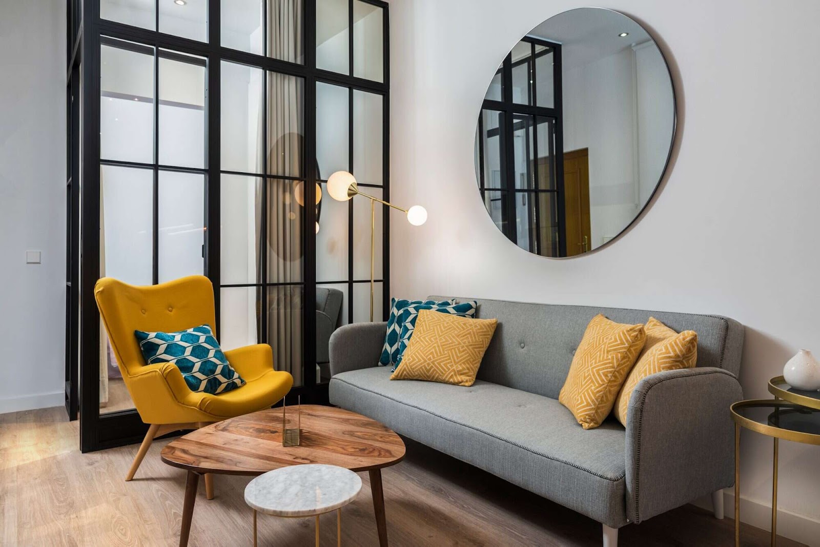 Colorful and cozy living room with a designer armchair and sofa along with a round decorative mirror and glass wall