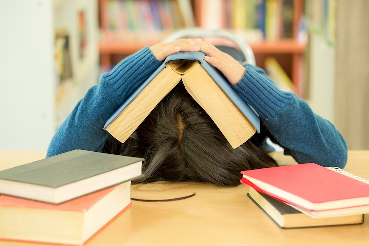 A student sitting in a college library, engrossed in reading an open book.