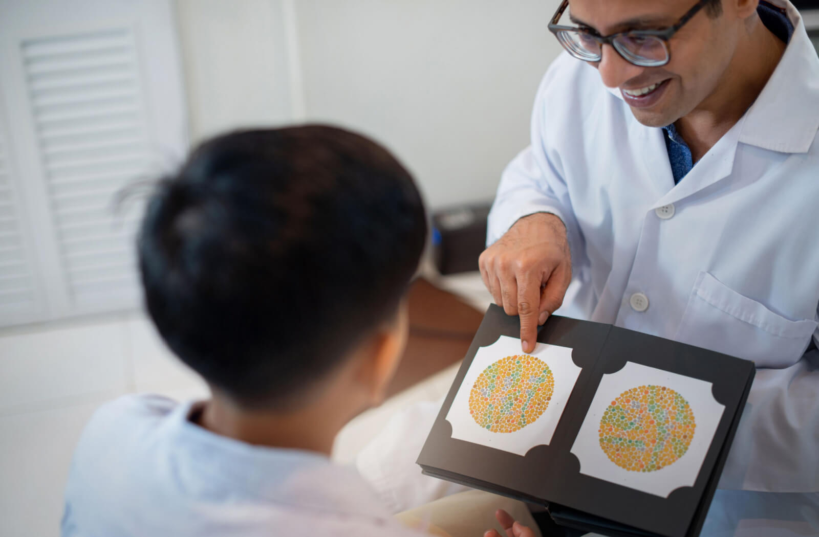 A male optometrist assesses a boy's vision skills through color vision testing.